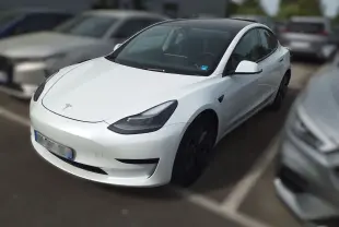 Tesla Model 3 blanc vue 3/4 avant droit, toit panoramique noir et jantes aérodynamiques noires visibles.