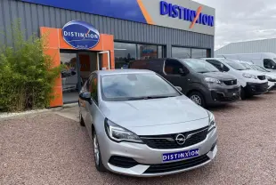 Opel Astra 1.2i Turbo gris argent vue 3/4 avant, avec calandre noire et phares LED, devant un garage Distinxion.