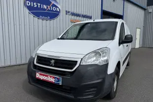 Peugeot Partner blanc vue 3/4 avant droit, avec pare-chocs noir mat et calandre distinctive, stationné devant un bâtiment industriel.