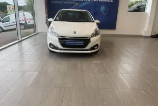 Peugeot 208 blanc banquise vue de face en intérieur avec calandre chromée et logo lion visible.