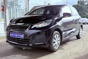 Peugeot 108 noire vue en 3/4 avant droit, avec calandre chromée et feux allumés, stationnée devant un bâtiment.