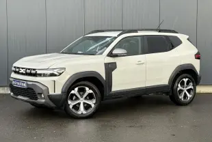 Vue 3/4 avant droit du Dacia Duster 2024 beige Sandstone avec barres de toit noires et jantes alliage distinctives.