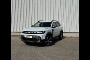 Dacia Duster blanc Glacier en 3/4 avant droit, avec jantes alu et barres de toit noires visibles.