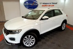 Volkswagen T-Roc blanc en 3/4 avant droit dans un showroom avec logo Distinxion en arrière-plan.