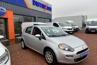 Fiat Grande Punto gris métallisé vue 3/4 avant droit avec phares allumés sur parking de concession.