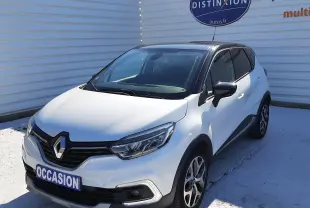 Renault Captur blanc nacré avec toit noir, vue 3/4 avant droit, sur parking devant un mur blanc.