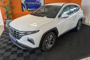 Hyundai Tucson blanc en 3/4 avant droit, avec jantes alliage et calandre chromée dans un showroom.