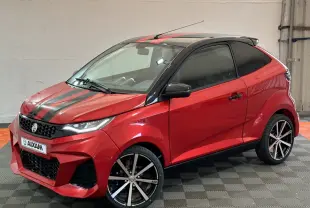 Vue 3/4 avant droit d'une Aixam Ambition rouge 2026 avec bandes noires sur le capot et jantes alliage noires.