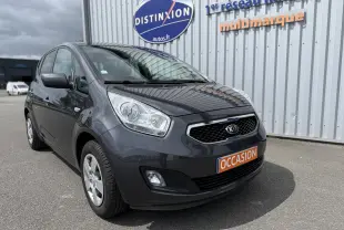 KIA Venga gris vue 3/4 avant droit, stationnée devant un bâtiment avec panneau Distinxion et plaque occasion.