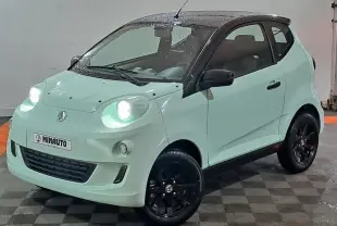 Vue 3/4 avant d'une Aixam Minauto E chic 2026 vert clair avec toit noir et jantes noires, phare avant allumé.