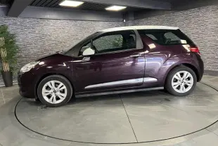 Profil côté gauche d'une DS3 violet avec toit blanc, jantes alliage et poignées chromées en intérieur showroom.