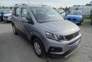 Peugeot Rifter gris Artense vu en 3/4 avant droit, avec calandre noire et toit surélevé, stationné en extérieur.