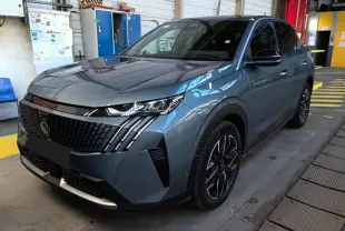Peugeot 3008 bleu en 3/4 avant droit dans un garage, avec calandre noire et phares LED distinctifs.