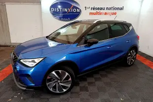 Vue 3/4 avant droite d’un SEAT Arona bleu 2022 avec toit noir et jantes alliage distinctives dans un showroom.