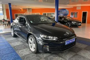 Volkswagen Scirocco noir vue 3/4 avant droit dans un showroom avec sol gris et bleu et mur orange.