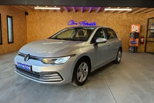 Volkswagen Golf gris clair vue 3/4 avant droit dans un showroom avec éclairage intérieur et panneau publicitaire.