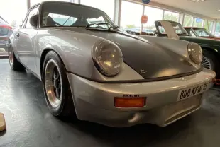 Porsche 911 3.0 SC gris métallisé vue 3/4 avant avec capot noir mat et jantes Fuchs noires.