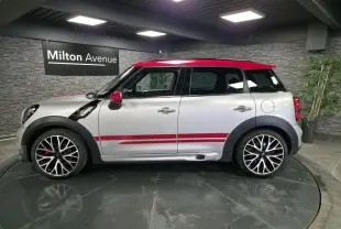 Profil droit d'une MINI Countryman gris clair avec toit et coques de rétroviseurs rouges et bandes sport rouges sur les portes.