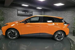 Profil droit d'une MG4 électrique orange avec toit noir et jantes alliage bi-ton dans un showroom intérieur.