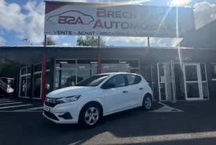 Vue 3/4 avant gauche d'une Dacia Sandero blanche 2024 garée devant un garage Brech Automobiles.