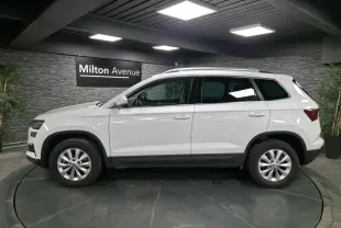 Profil côté gauche d'un SUV SKODA KAROQ blanc 2024 dans un showroom avec jantes alliage 16 pouces.