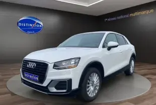 Audi Q2 blanc en 3/4 avant droit, mettant en valeur sa calandre noire et ses jantes alliage sur fond intérieur showroom.