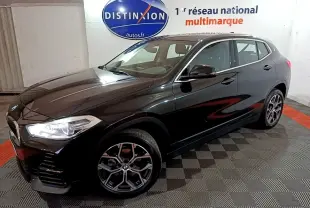 BMW X2 sDrive18i Lounge noir en 3/4 avant droit, avec jantes alliage et phares LED allumés dans un showroom.