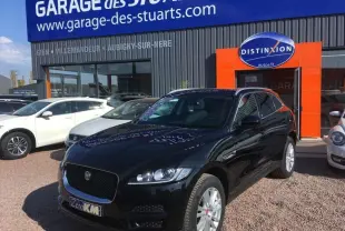 Jaguar F-PACE noir en 3/4 avant droit garé devant un garage avec jantes argentées et calandre noire.