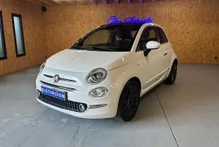 Fiat 500 blanc crème vue 3/4 avant droit dans un intérieur avec mur en bois et jantes noires.