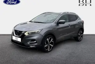 Nissan Qashqai gris Squale en 3/4 avant droit, avec jantes alliage noires et barres de toit visibles.