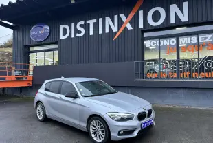 BMW Série 1 F20 blanche vue en 3/4 avant droit devant un bâtiment noir avec enseigne Distinxion.