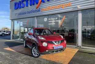Nissan Juke rouge 2017 en 3/4 avant droit, avec jantes alliage et calandre distinctive devant un showroom multimarque.