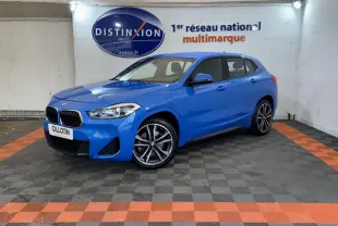 BMW X2 xDrive25e M Sport bleu en 3/4 avant droit dans un showroom avec sol gris et bandes orange.