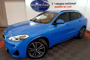 BMW X2 sDrive20i M Sport bleu en vue 3/4 avant droit, avec jantes sport et vitres teintées, intérieur beige visible.