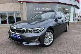 BMW Série 3 330eA Mineralgrau vue 3/4 avant droit, avec jantes alliage et calandre chromée devant un showroom Distinxion