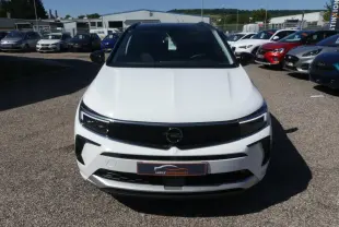 Vue avant d'un Opel Grandland blanc métallisé avec calandre noire brillante et phares LED, sur un parking extérieur.
