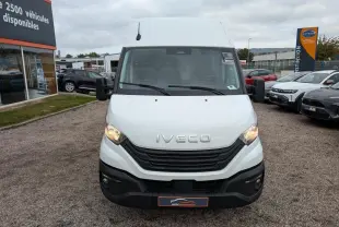 Vue avant d'un utilitaire Iveco Daily blanc avec calandre noire et phares allumés sur un parking.