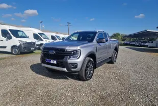 Ford Ranger Super Cabine gris Iconic vu en 3/4 avant droit sur un parking extérieur sous un ciel bleu.