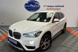 BMW X1 sDrive18iA blanc en 3/4 avant droit avec jantes bi-ton et hayon électrique visible en arrière-plan.