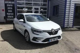Renault Mégane IV Société blanche vue en 3/4 avant droit, stationnée devant un garage avec panneaux de service.