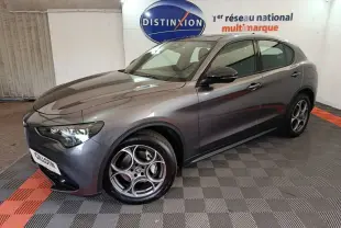Alfa Romeo Stelvio gris foncé en 3/4 avant droit, avec phares LED et jantes distinctives à cinq cercles.