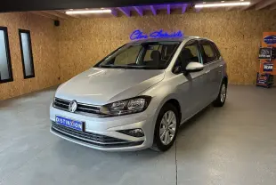 Volkswagen Golf Sportsvan gris vue 3/4 avant droit dans un showroom avec mur en bois et enseigne lumineuse bleue.