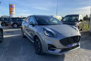 Ford Puma gris en 3/4 avant droit sur parking, avec calandre noire et jantes classiques visibles.