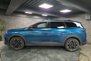 Profil droit d'un Peugeot 5008 bleu métallisé 2025 avec jantes alliage 19'' noires et barres de toit noires brillantes.