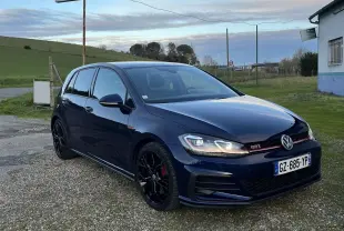 Volkswagen Golf VII GTI Performance bleu lapiz métal vue 3/4 avant droit sur parking gravier.