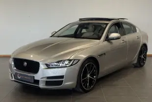 Jaguar XE beige vue 3/4 avant droit avec toit ouvrant et jantes noires en intérieur showroom.