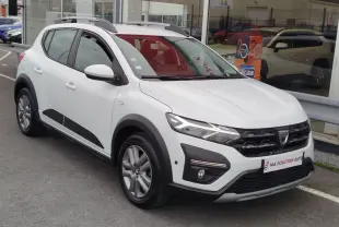 Vue 3/4 avant d'une Dacia Sandero Stepway blanche glacier avec détails noirs et barres de toit grises.