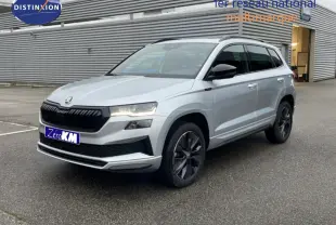 Vue 3/4 avant d'un Skoda Karoq gris argent métallisé avec jantes noires et calandre noire, stationné devant un bâtiment industriel.