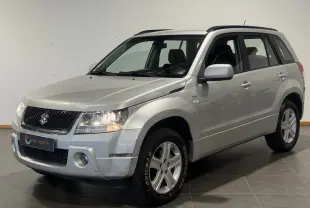 Suzuki Grand Vitara gris en 3/4 avant droit, SUV 2007 avec jantes alliage et barres de toit visibles.