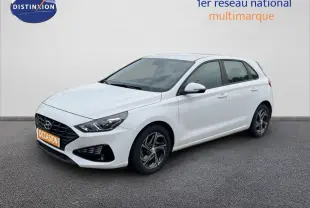 Hyundai i30 blanc nacré vue 3/4 avant droit, compacte 5 portes avec jantes alliage et calandre noire distinctive.